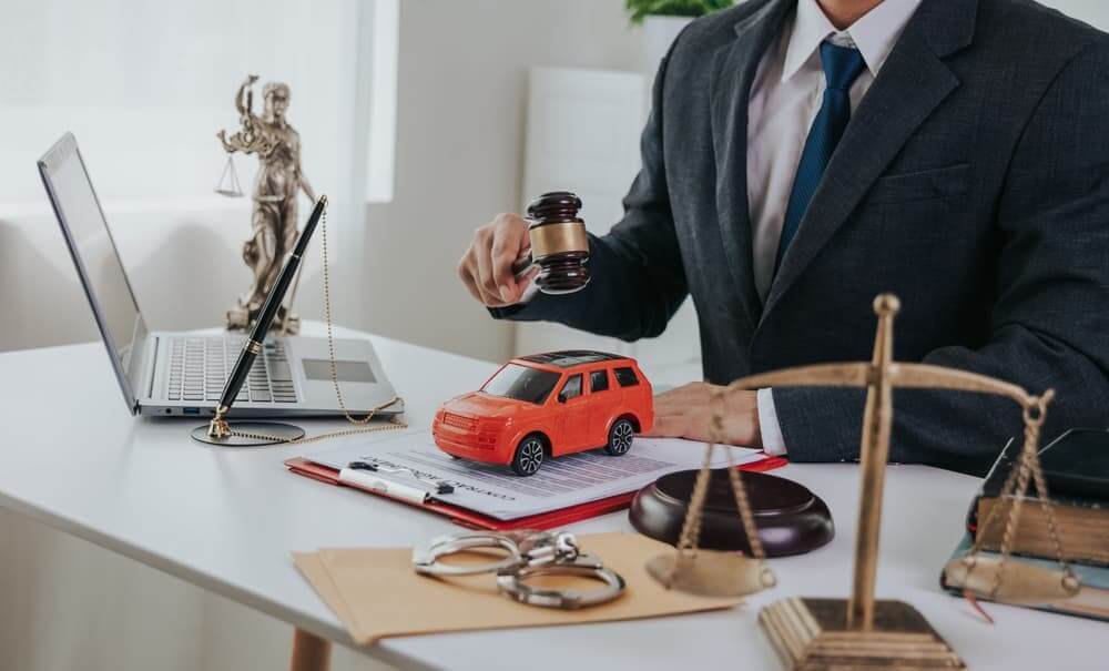 A male judge's hand is depicted holding a car, documents, and a hammer.