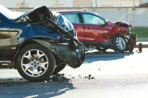 Two vehicles collide on the street, resulting in a car crash with damaged automobiles. 