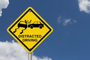 A yellow warning sign with the words "Distracted Driving" and an icon depicting an accident against a sky background.