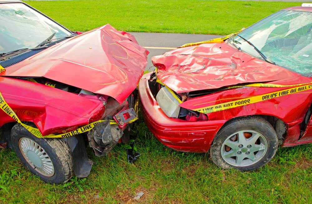 Two fiery red cars, their hoods crumpled and windshields shattered, locked in a devastating head-on collision. The scene is a symphony of chaos and destruction, with metal twisted and glass strewn across the asphalt.