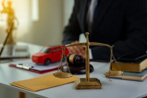 A lawyer sitting at a desk with a justice scale and a car