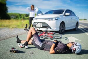 An unconscious male cyclist lies on the road after a traffic accident, with selective focus highlighting the severity of the situation.