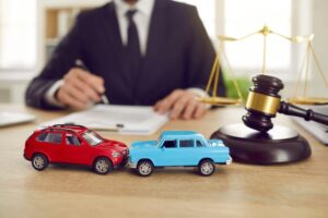 A close-up of two toy model cars symbolizing an accident, positioned on a table in front of a judge presiding over a car accident lawsuit.