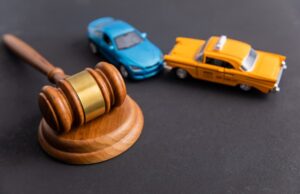 A judge's gavel sits beside two toy cars colliding, symbolizing a traffic accident, with legal proceedings in the background, representing justice in accident cases.