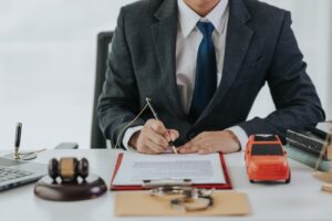 A male judge's hand holds a toy car with legal documents and a gavel nearby, symbolizing a car accident case in court. 