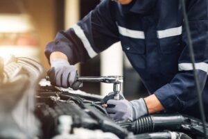 A mechanic works on a car's engine in the garage, representing car inspection and repair services. 