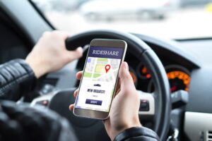 A rideshare driver in his car, using a mobile phone to check the rideshare app. A new taxi ride request pops up on the smartphone as he prepares to pick up passengers. 