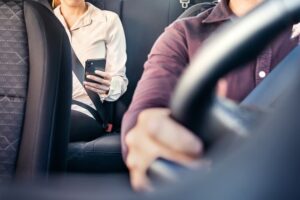 The taxi driver focuses on the road, while the passenger interacts with her smartphone, possibly tracking the ride or sending messages.