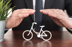 An insurer shields a bicycle with both hands, symbolizing protection and coverage for cyclists.