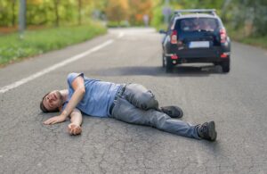 Hit and run concept: An injured man lies on the road in front of a car, highlighting the severity of the accident.