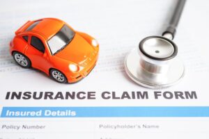 A stethoscope placed on an insurance claim form for a car accident, symbolizing the connection between health and auto insurance, alongside concepts of car loans, insurance, and leasing.