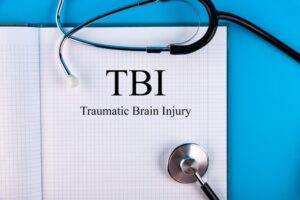 TBI (Traumatic Brain Injury) written in a notebook placed on a desk alongside a stethoscope, representing a medical concept.