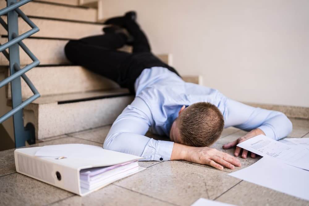 Person lying on a staircase after slipping and falling, with legs extended and one shoe partially off, conveying the impact of the accident. The scene highlights the dangers of stair-related slip and fall accidents.