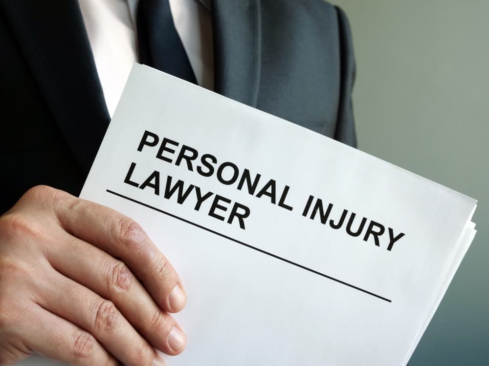 Image of a personal injury lawyer in professional attire holding a clipboard with legal documents, standing beside a bookshelf filled with law books. The lawyer appears focused and attentive, symbolizing thorough case preparation and knowledge of legal principles. The clipboard and law books highlight their dedication to handling personal injury cases with attention to detail and expertise.