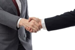 Close-up image of two business professionals shaking hands against a plain white background, symbolizing successful cooperation and partnership. Both individuals wear business attire, suggesting a formal agreement or collaboration. The clean, minimalist background emphasizes the handshake as a gesture of trust, teamwork, and mutual success.