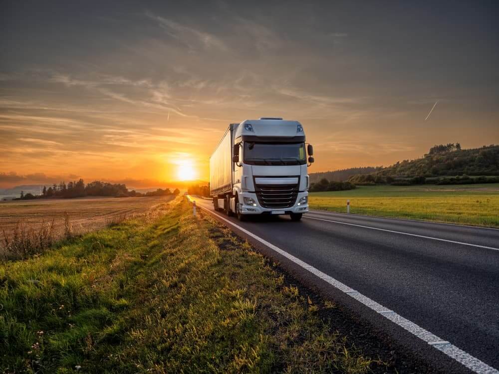 White truck driving on the asphalt road in rural landscape at sunset