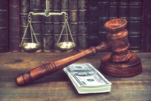 Judge Gavel, Scale Of Justice With USa Dollars And Law Book On Judges Table In Courtroom