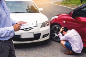 Insurance agent writing on clipboard while inspecting damaged car after accident, assessing claim for uninsured driver case. 