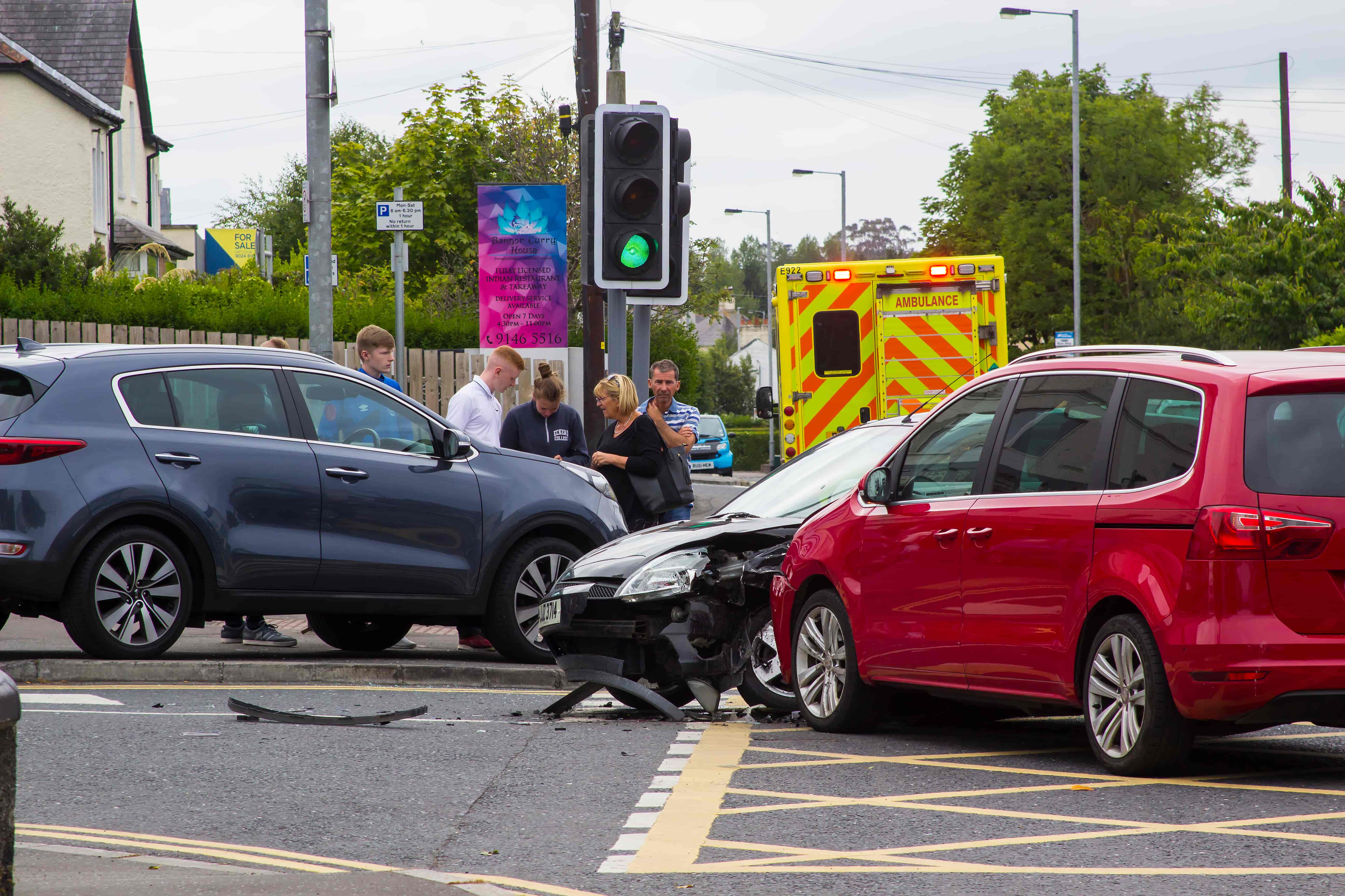 Car accident at intersection with ambulance on scene and people discussing damages.