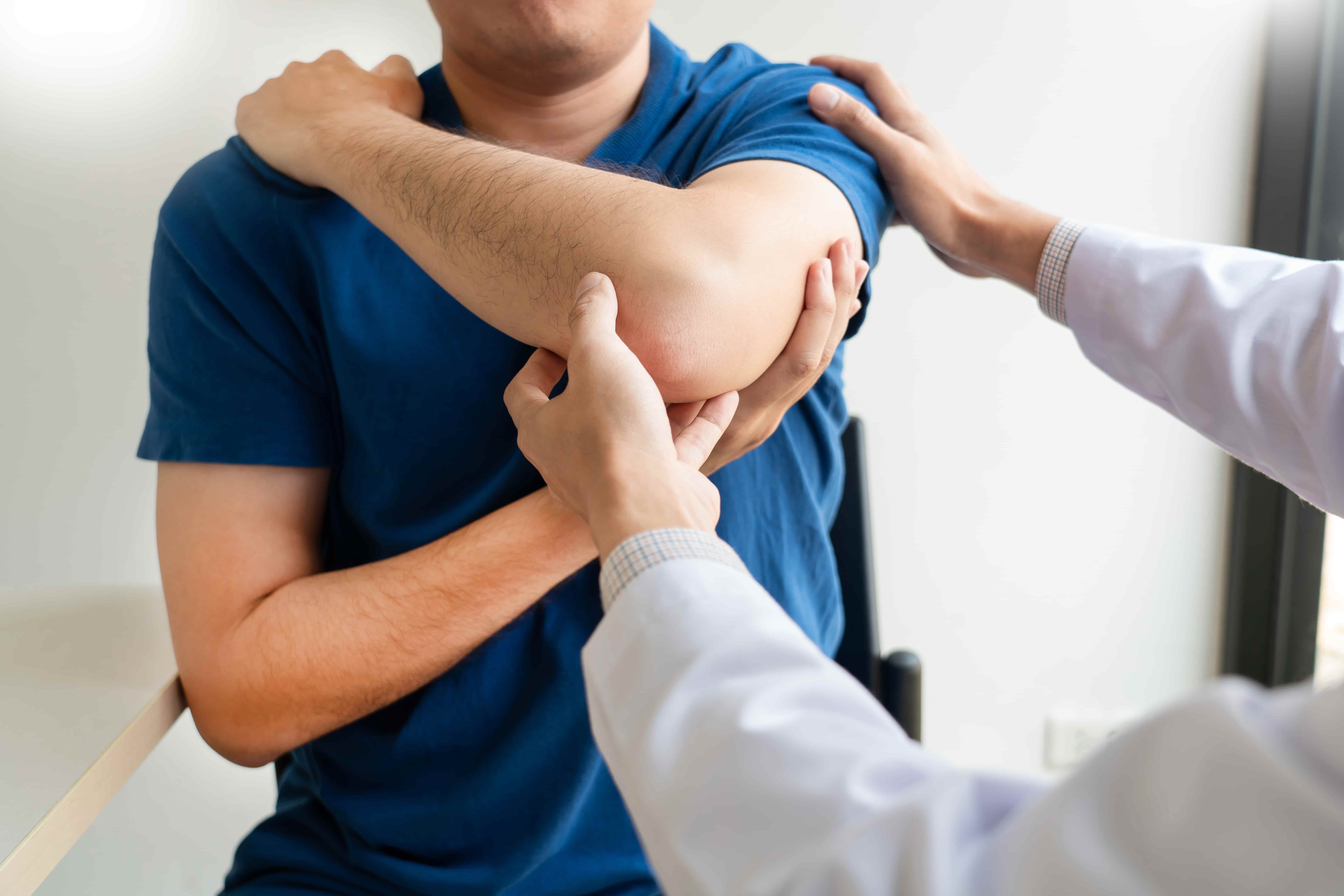 Doctor examining patient’s injured elbow during medical consultation and treatment.