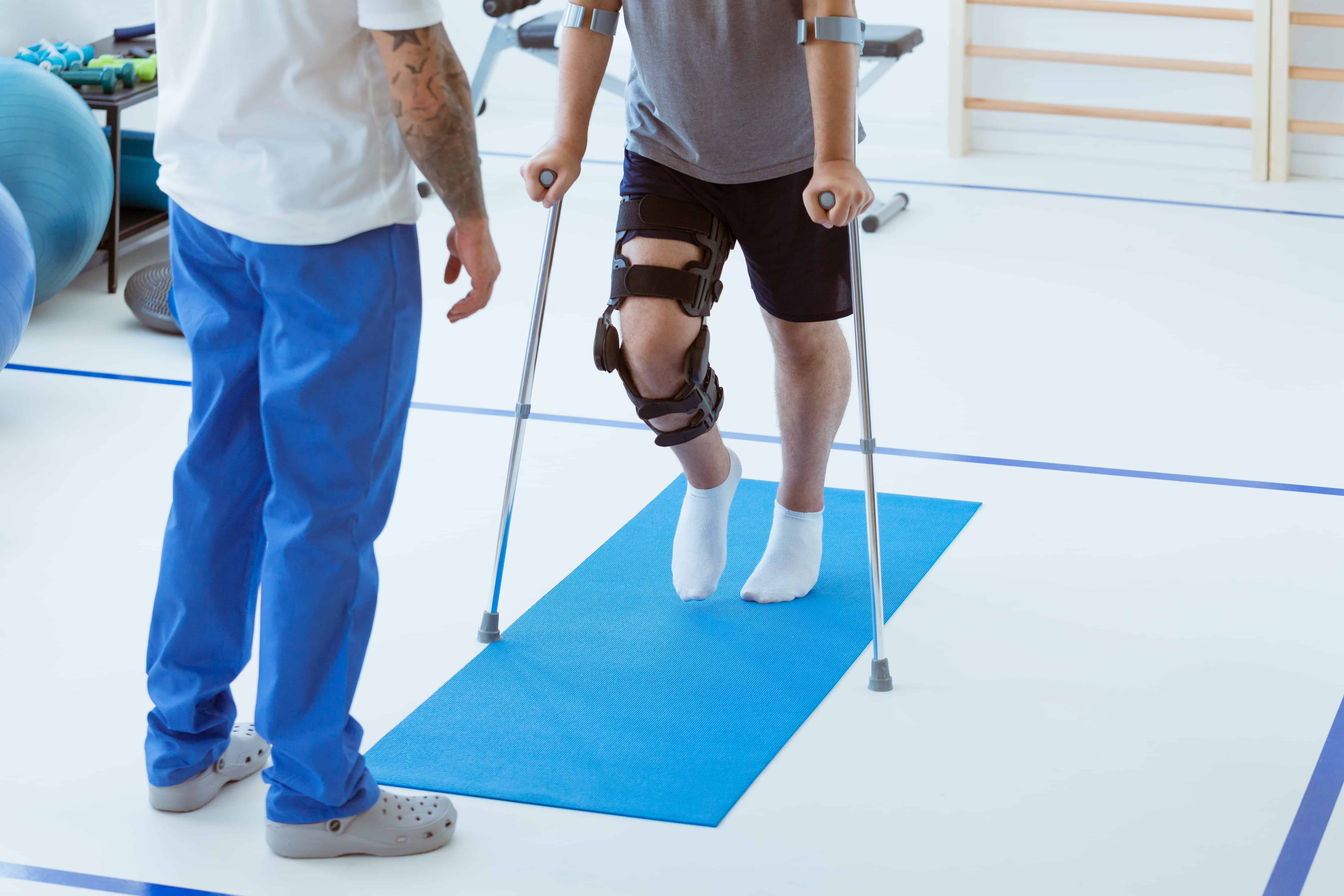 Injured man with leg brace using crutches during physical therapy rehabilitation session.