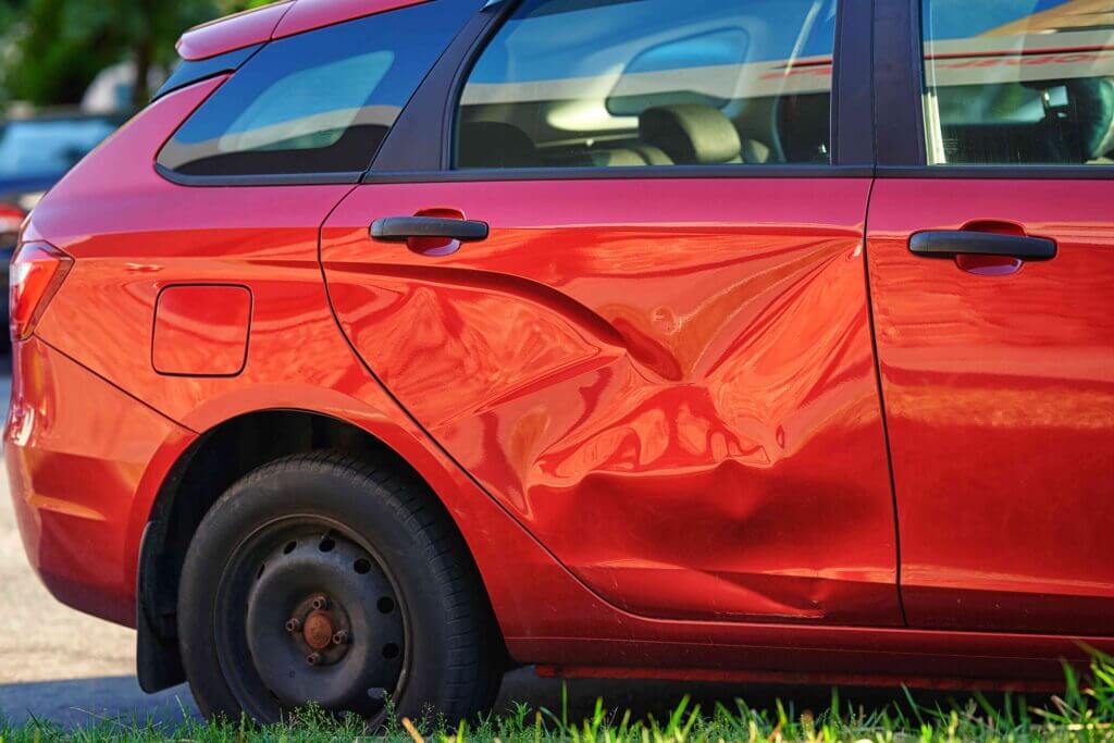 Red car with a large dent on the side door after a collision.