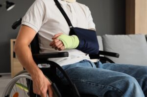 Motorcycle accident injury victim sitting in a wheelchair with a cast and arm sling, recovering and seeking disability compensation.