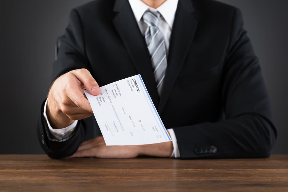 Businessman in a suit handing over a settlement check representing a lowball insurance offer after an accident claim.