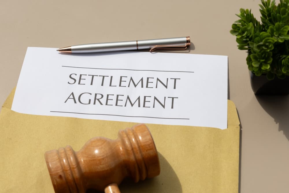 Settlement agreement document with pen and judge’s gavel on a desk.